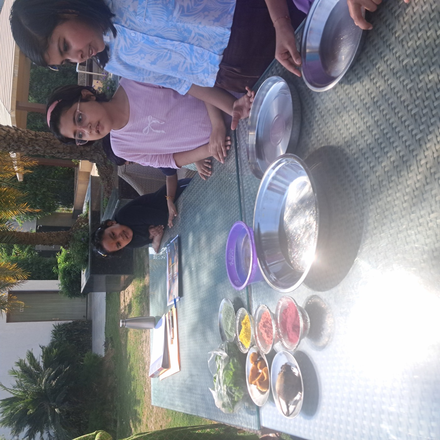 Children around a garden table with bowls of natural Holi powders, turmeric roots, beetroot, and leafy greens