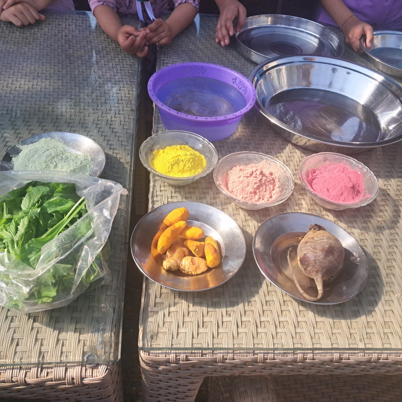 Top view of turmeric, beetroot, spinach leaves, and bowls of yellow, pink, and green powder