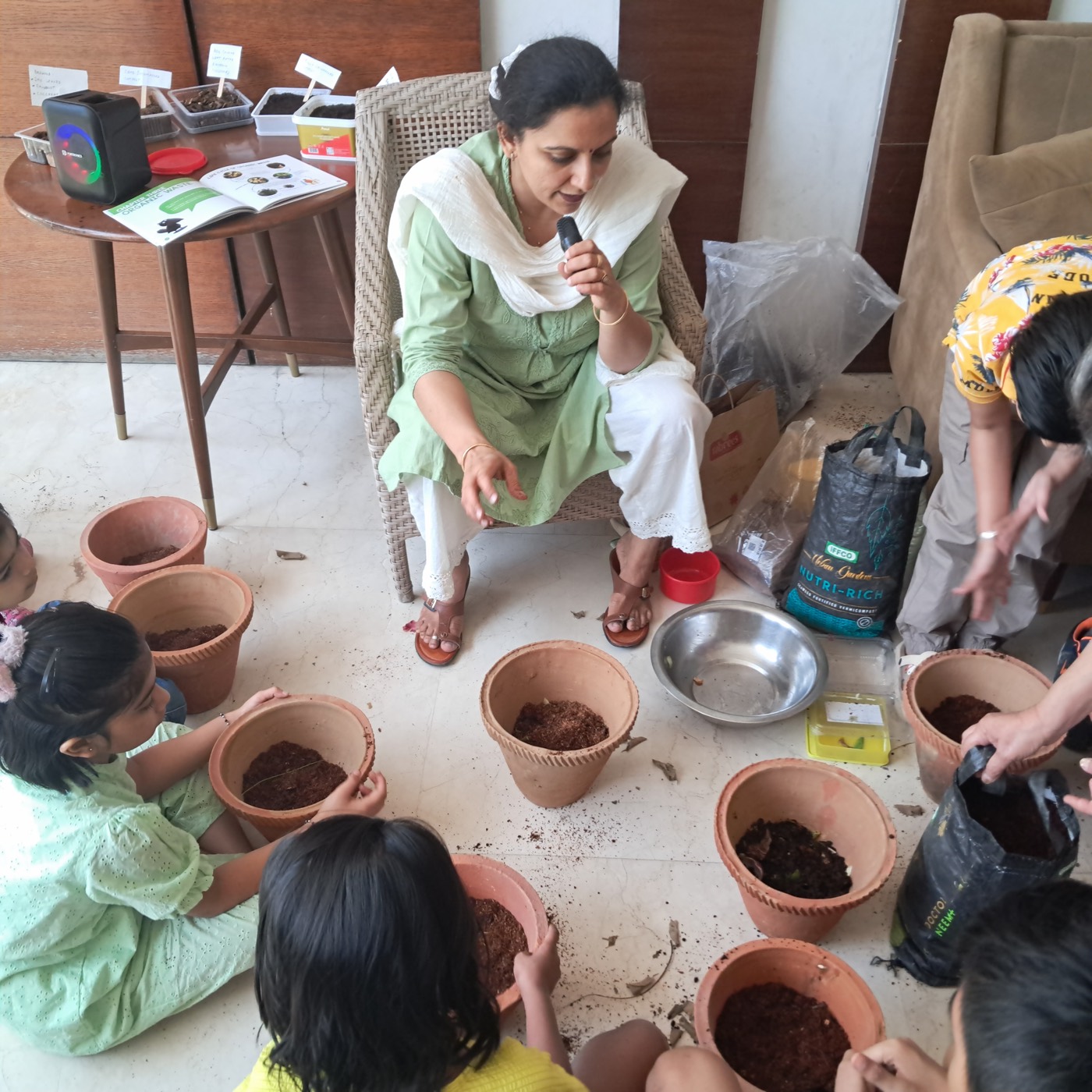Children sitting on the floor filling terracotta pots with compost while the facilitator speaks